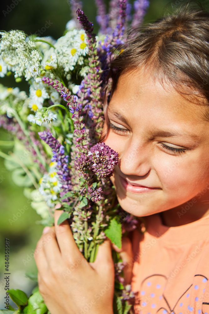A school-age girl is holding a large bouquet of various wild flowers of different colors and types. A school-age girl is holding a large bouquet of various wild flowers of different colors and types.