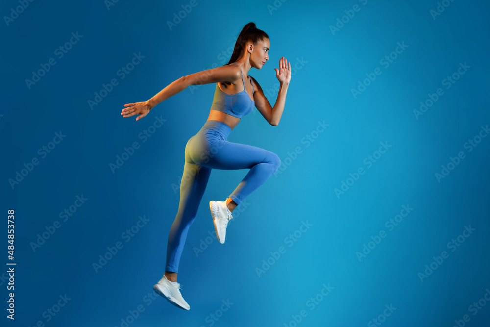 Sporty Woman Exercising Doing Elbow-To-Knee Crunch Standing On Blue Background