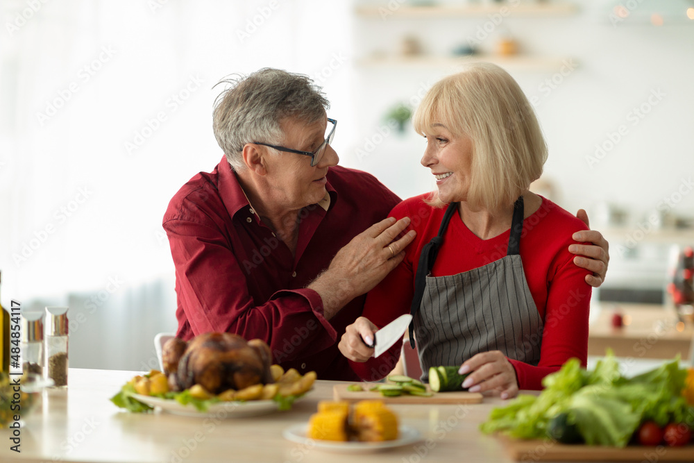 Loving senior couple looking at each other while preparing traditional roasted turkey for Christmas dinner at home
