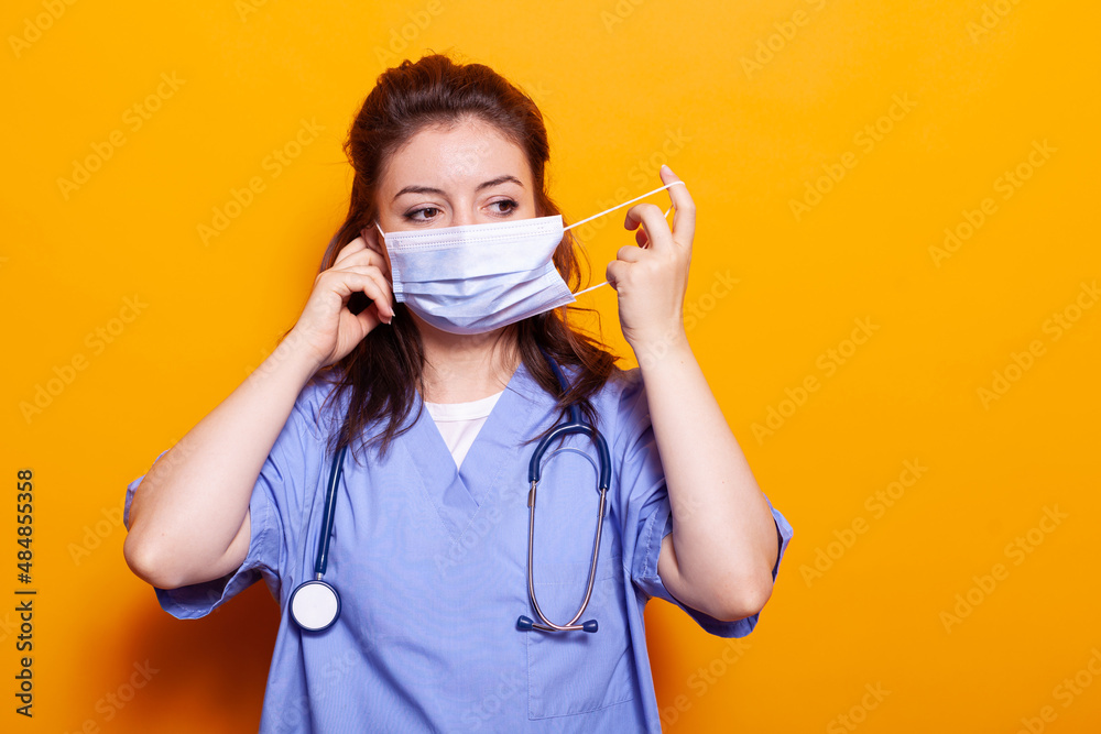 Medical assistant putting protective mask on face in front of camera. Woman nurse wearing uniform and stethoscope, having safety and protection against coronavirus during pandemic. Medical assistant putting protective mask on face in front of camera. Woman nurse wearing uniform and stethoscope, having safety and protection against coronavirus during pandemic.
