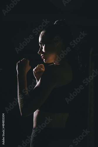 Young woman boxer in the dark in contour light. Side view. Vertical composition