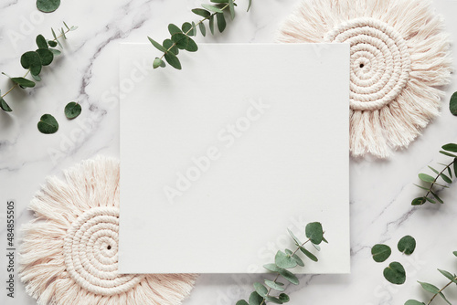 Mockup with blank square canvas, copy-space. Eucalyptus twigs, macrame pads.Winter flat lay background . Top view on white marble photo