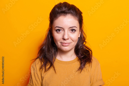 Portrait of positive woman standing in photography studio, looking at camera to pose for pictures. Caucasian person with cheerful look standing over isolated orange background. © DC Studio
