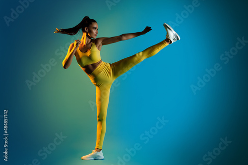 Woman Doing Karate Side Kick Raising Leg Clenching Fists, Studio