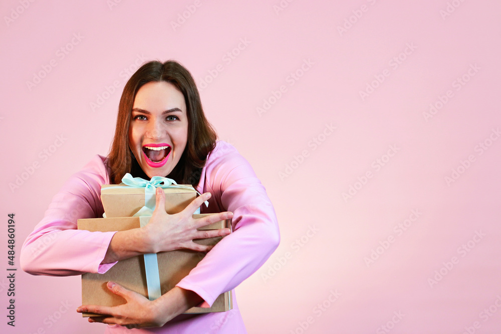 Studio shot of young beautiful positive brunette women in pink dress on pink background. Holding present with blue ribbon.