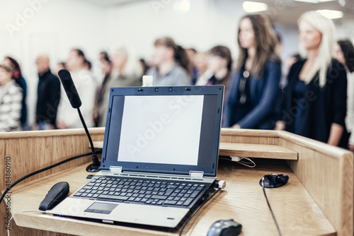 Canvas Print Laptop and microphone on the rostrum in lecture hall full of conference participants