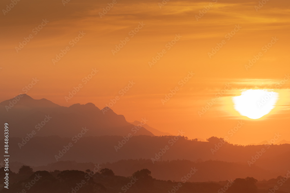 BEAUTIFUL ORANGE SUNSET WITH MEADOWS AND MOUNTAINS IN THE BACKGROUND