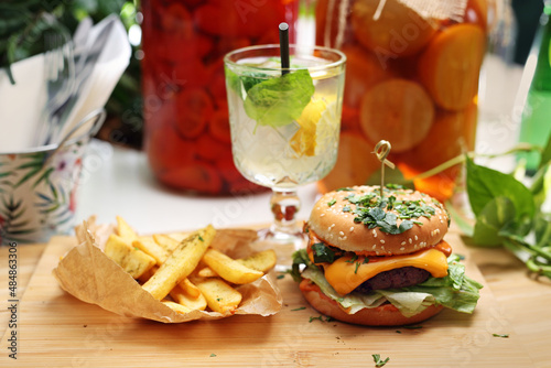 Vege cheeseburger, potato fries and lemonade on a wooden cutting board. Vegan lunch set. Plant-based meal.
