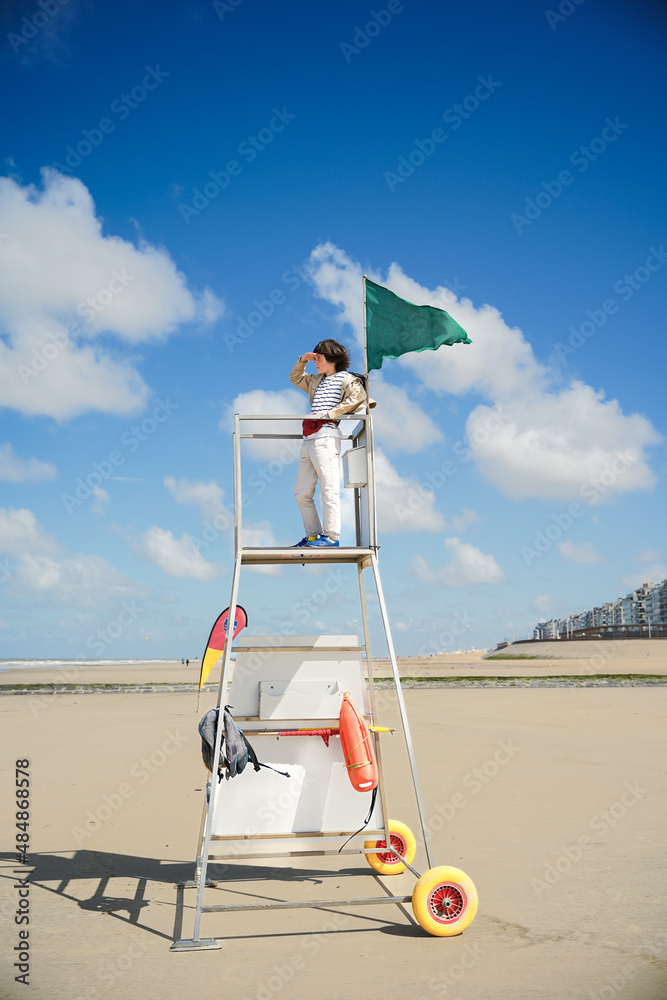 Boy is staying on rescue tower looking into the distance at the sea ...