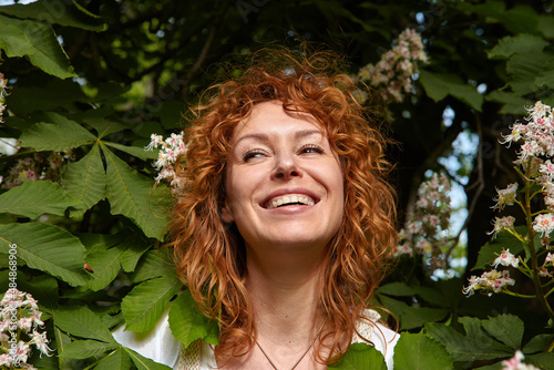 Portrait of beautiful red hair woman with beaming smile among the flowers of chestnut.