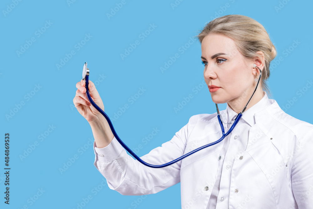 Female doctor smiling holding a stethoscope in her hands on a blue background. Hospital. Treatment. Listen to the rhythm of the heart. Female doctor smiling holding a stethoscope in her hands on a blue background. Hospital. Treatment. Listen to the rhythm of the heart.