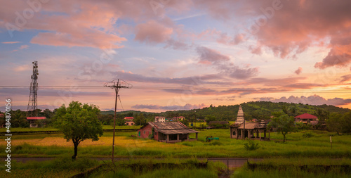 Traditional Indian village house and temple surrounded by green grass and beautiful sunset view photo