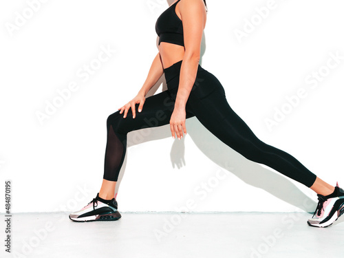 Portrait of fitness confident woman in black sports clothing. Sexy young beautiful model with perfect body. Female isolated on white wall in studio. Stretching out before training. No face