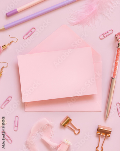 Pink paper card with envelope near school girly stationery on pink Top view