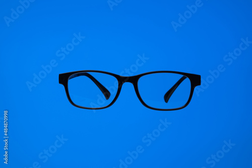 Black plastic frame eyeglasses. Close up studio shot, isolated on blue background, no people