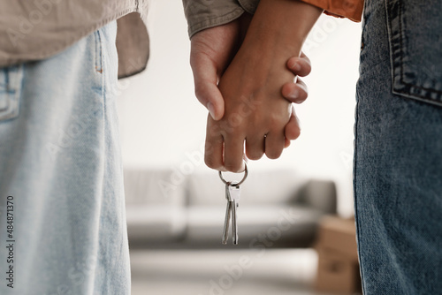 Cropped view of millennial couple holding hands and key to new home, moving in together. Mortgage for young families