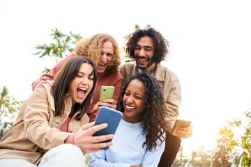 Happy friends watching screen mobile phone with a surprised face and smiling. Young adult people using smartphone and having fun.