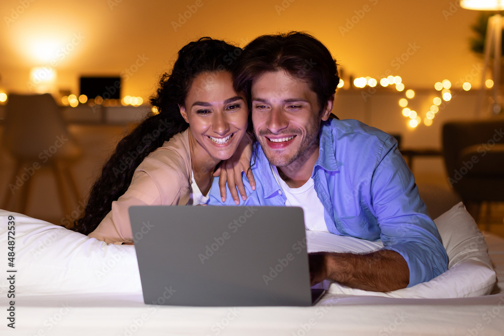 Smiling Couple Using Laptop Watching Funny Film In Bedroom Smiling Couple Using Laptop Watching Funny Film In Bedroom
