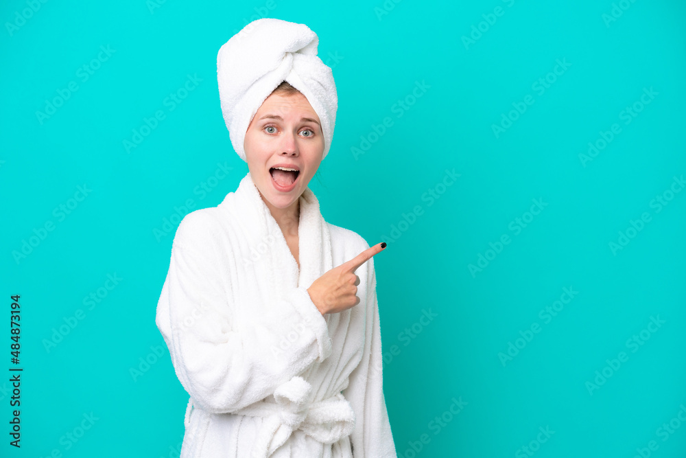 Young woman in a bathrobe isolated on blue background surprised and pointing side Young woman in a bathrobe isolated on blue background surprised and pointing side