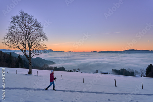senior woman, sno hiking in sunset in the Bregenzer Wald area of Vorarlberg, Austria with spectacular view on Mount Saentis over sa sea of fog, Switzerland 
