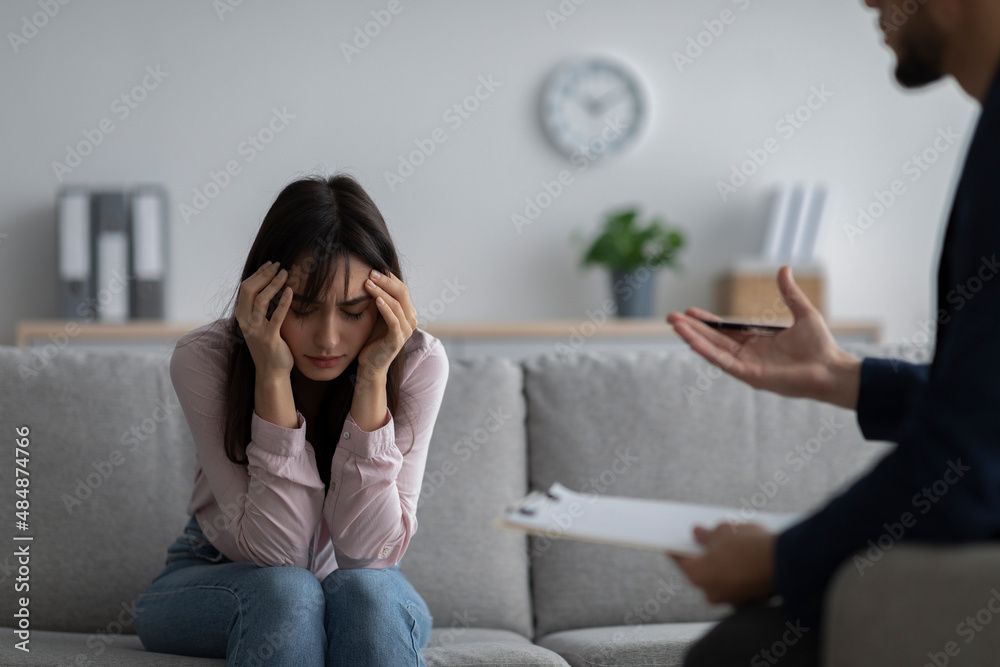 Depressed young woman touching head, seeking professional help with mental disorder at psychotherapist's office Depressed young woman touching head, seeking professional help with mental disorder at psychotherapist's office