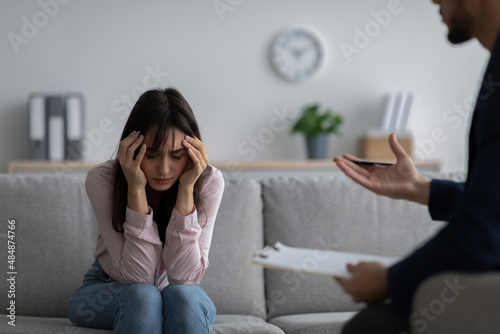 Depressed young woman touching head, seeking professional help with mental disorder at psychotherapist's office