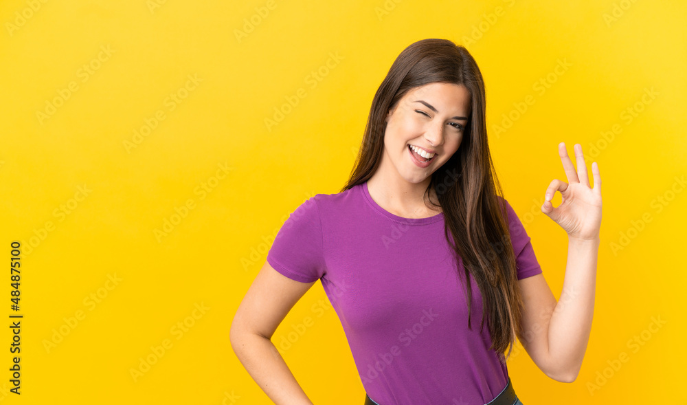 Teenager Brazilian girl over isolated yellow background showing ok sign with fingers Teenager Brazilian girl over isolated yellow background showing ok sign with fingers