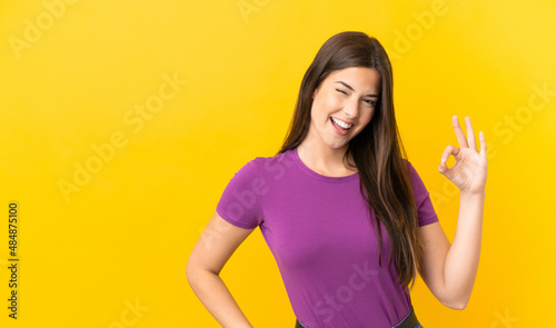 Teenager Brazilian girl over isolated yellow background showing ok sign with fingers