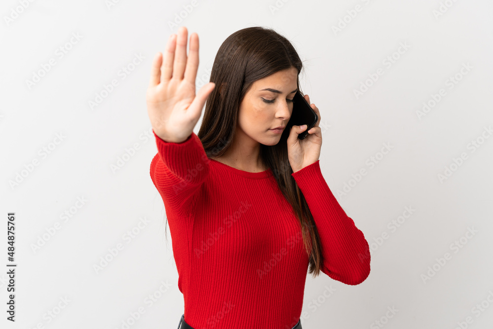 Teenager Brazilian girl using mobile phone over isolated white background making stop gesture and disappointed Teenager Brazilian girl using mobile phone over isolated white background making stop gesture and disappointed