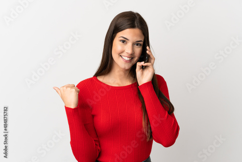 Teenager Brazilian girl using mobile phone over isolated white background pointing to the side to present a product