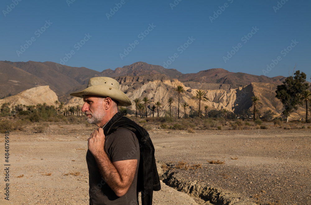 Adult man in cowboy hat on Tabernas desert with palm trees against blue sky. Almeria, Spain Adult man in cowboy hat on Tabernas desert with palm trees against blue sky. Almeria, Spain