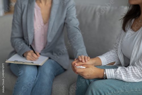 Female psychotherapist providing support to young woman, holding her hand at clinic, cropped photo