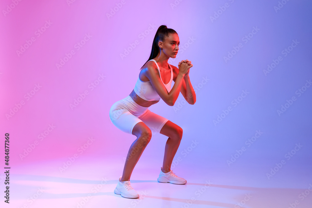 Woman Doing Deep Squat Exercising Over Neon Studio Background