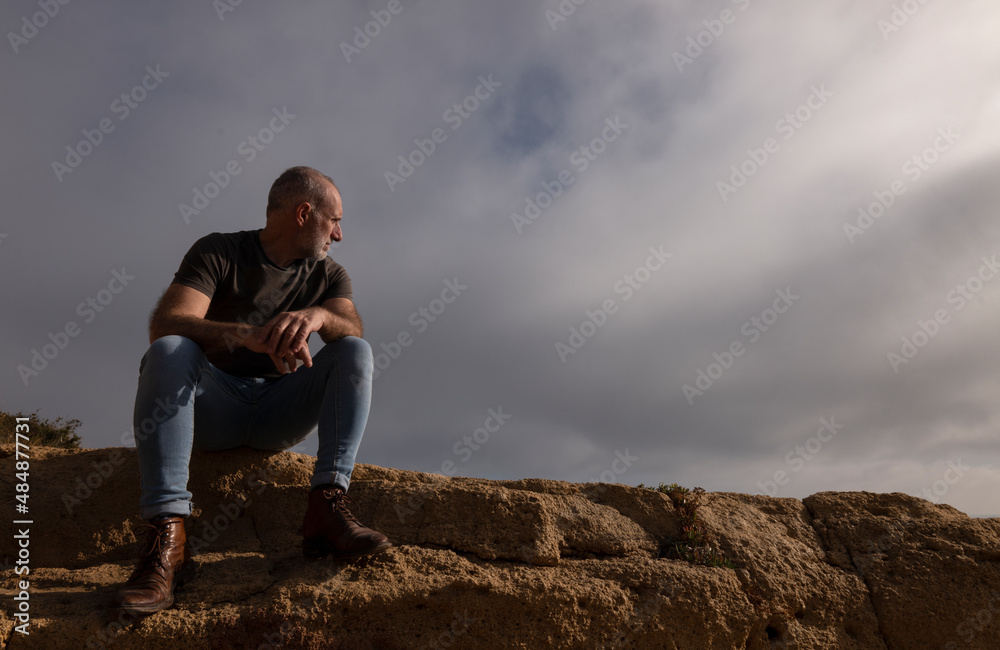Adult man sitting on cliff against sky. Almeria, Spain
