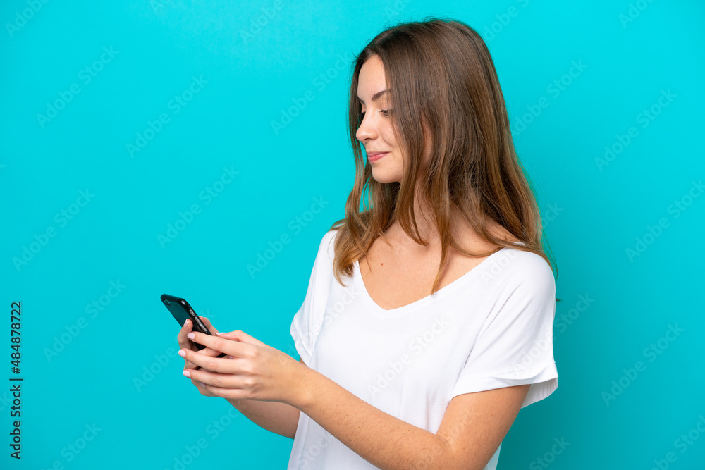 Young caucasian woman isolated on blue background sending a message or email with the mobile Young caucasian woman isolated on blue background sending a message or email with the mobile