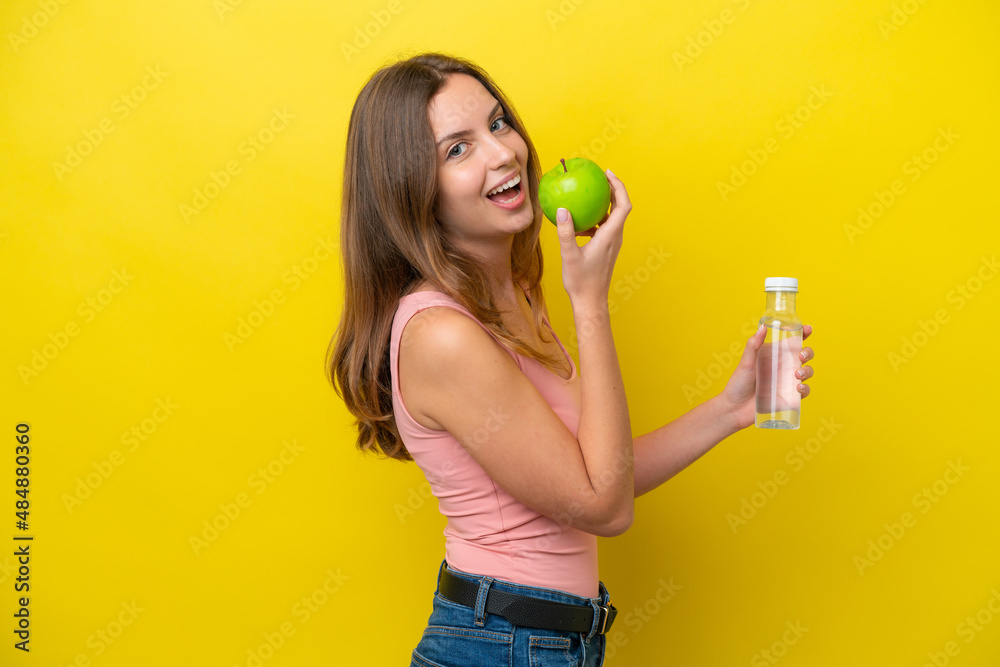 Young caucasian woman isolated on yellow background with an apple and with a bottle of water
