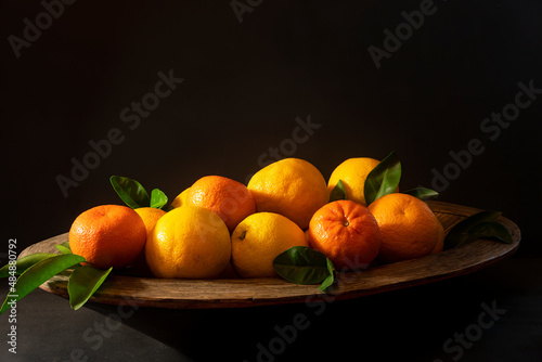 Wooden bowl of citrus fruit  oranges and mandarines  on a textured black background side lit with copy space.