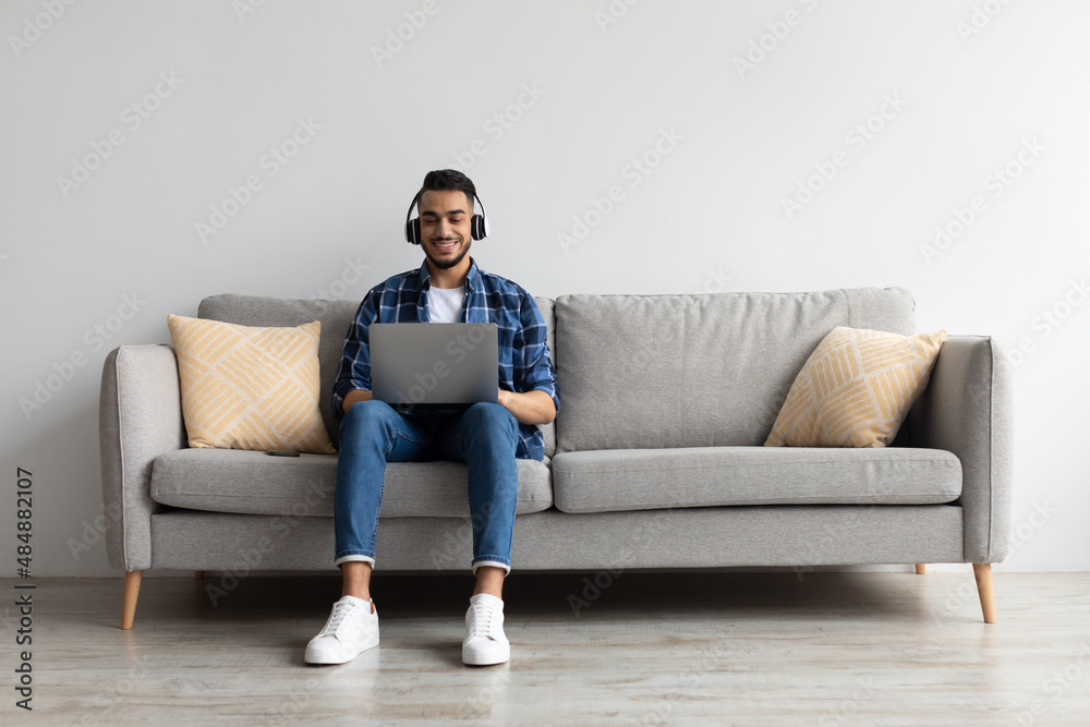 Smiling Arab man in headphones using pc at home Smiling Arab man in headphones using pc at home