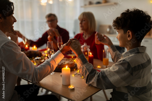 Religious multi generation family holding hands and praying before festive Christmas dinner at home, selective focus