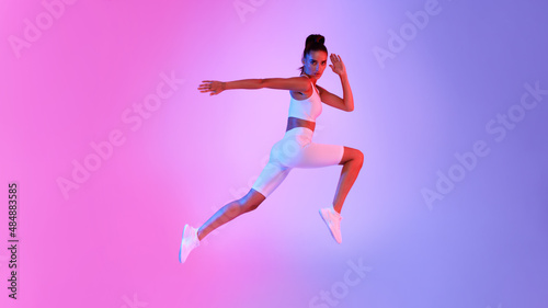 Athletic Female Jumping In Mid-Air Over Pink And Blue Background