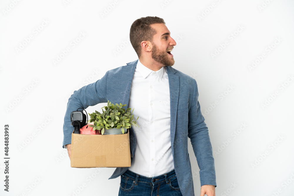 Young caucasian making a move while picking up a box full of things isolated on white background laughing in lateral position