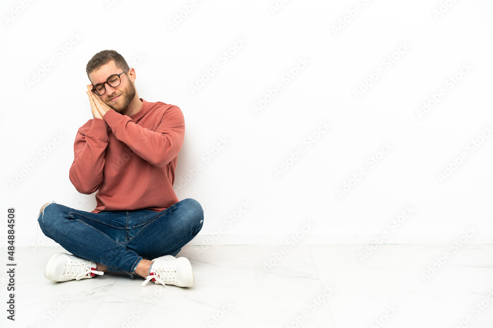 Young handsome man sitting on the floor making sleep gesture in dorable expression Young handsome man sitting on the floor making sleep gesture in dorable expression