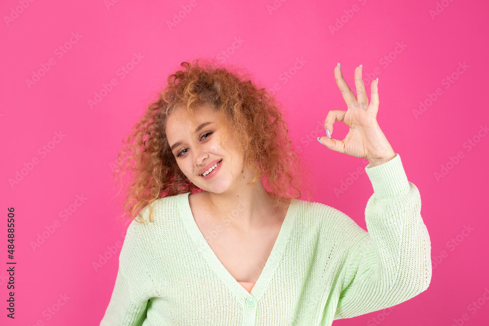 Young beautiful curly red-haired girl shows ok sign to the camera. A sign of success and good luck.