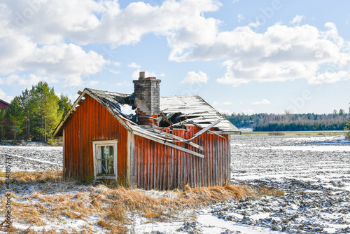 Old tiny cottage with collapsed roof by the field in the countryside in spring