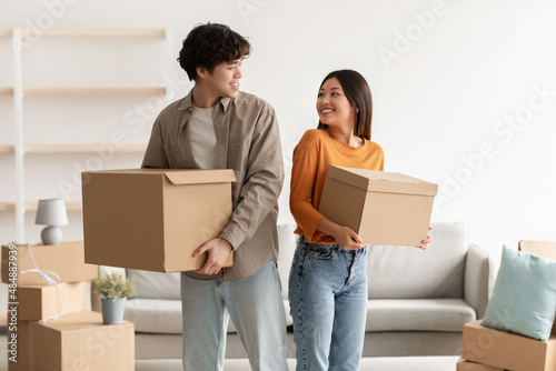 Home relocation concept. Positive young Asian couple carrying carton boxes in their owned house