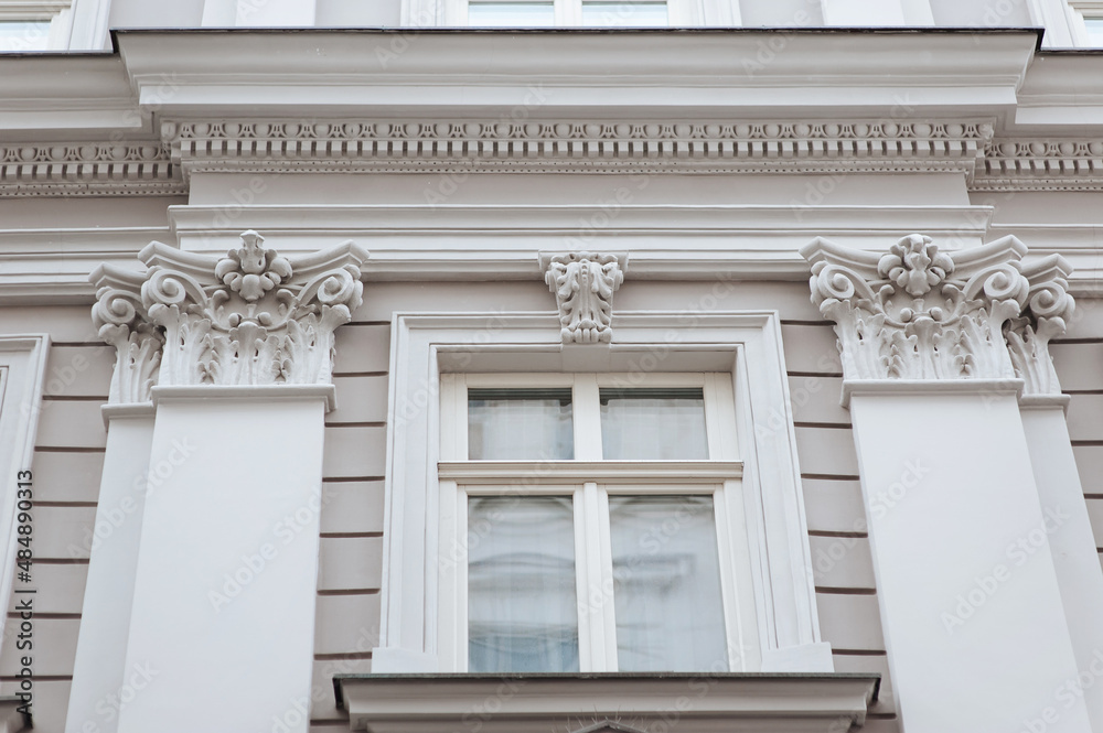 Window with wooden frame. Neoclassical building with a complex structure with pilasters and capitals in the Corinthian style. Light gray facade of an old house in Lviv, Ukraine.