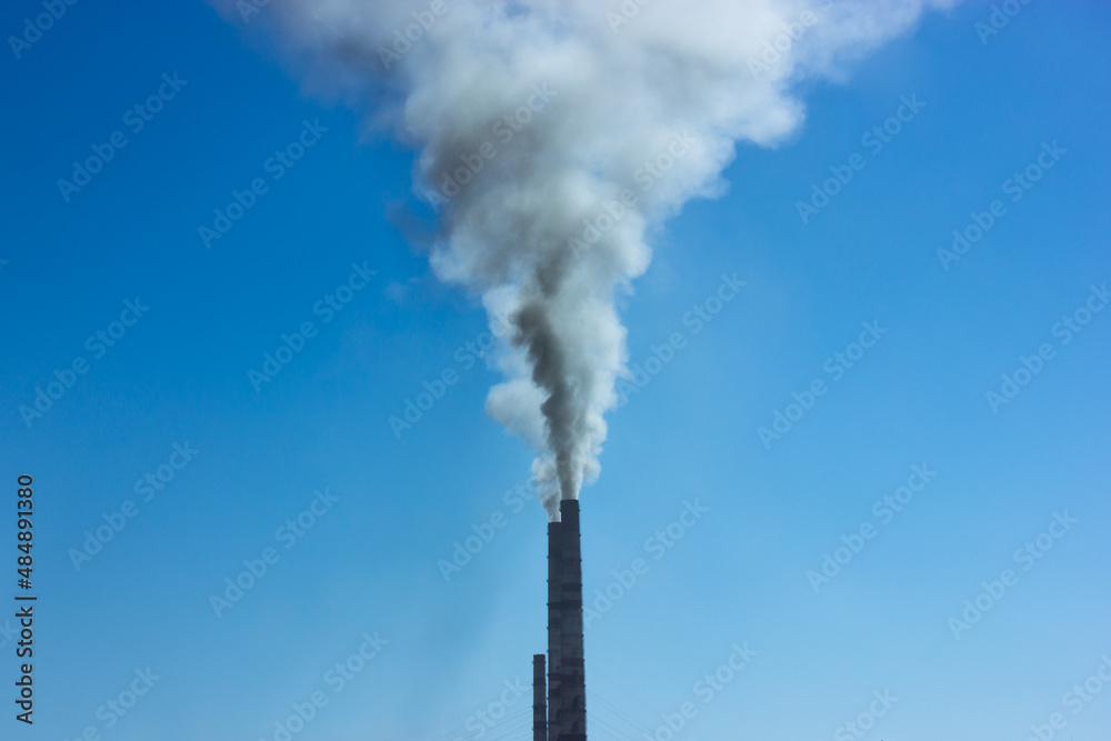 Chimney with smoke coming out of it against a blue sky in the industrial area. Environmental pollution, ecology problem. A high pipe with smoke moving up. Toxic carbon dioxide CO2 acidic colorless gas