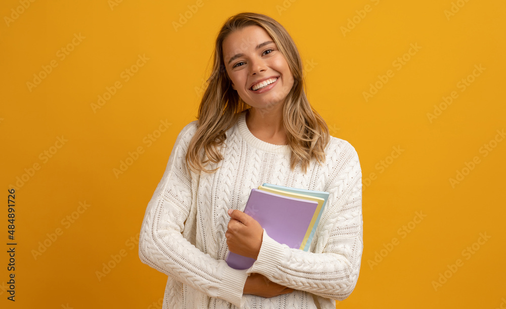young smiling pretty blond woman posing with books on yellow studio background isolated, happy education, wearing white sweater young smiling pretty blond woman posing with books on yellow studio background isolated, happy education, wearing white sweater