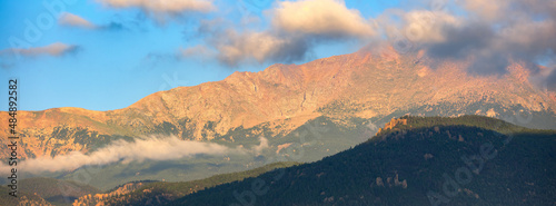 Panoramic image of sunrise striking Pikes Peak in Colorado as low lying clouds hover near the mountain