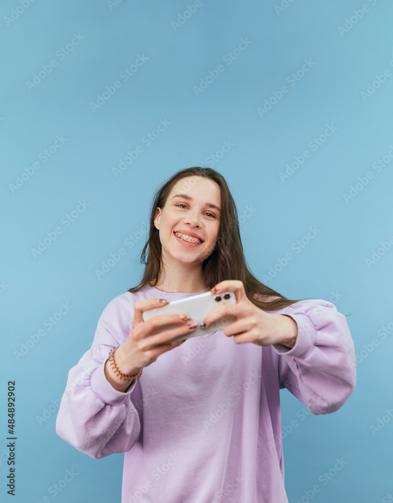 Happy girl gamer with smartphone in hands isolated on blue background, looks at camera and smiles. Happy girl gamer with smartphone in hands isolated on blue background, looks at camera and smiles.